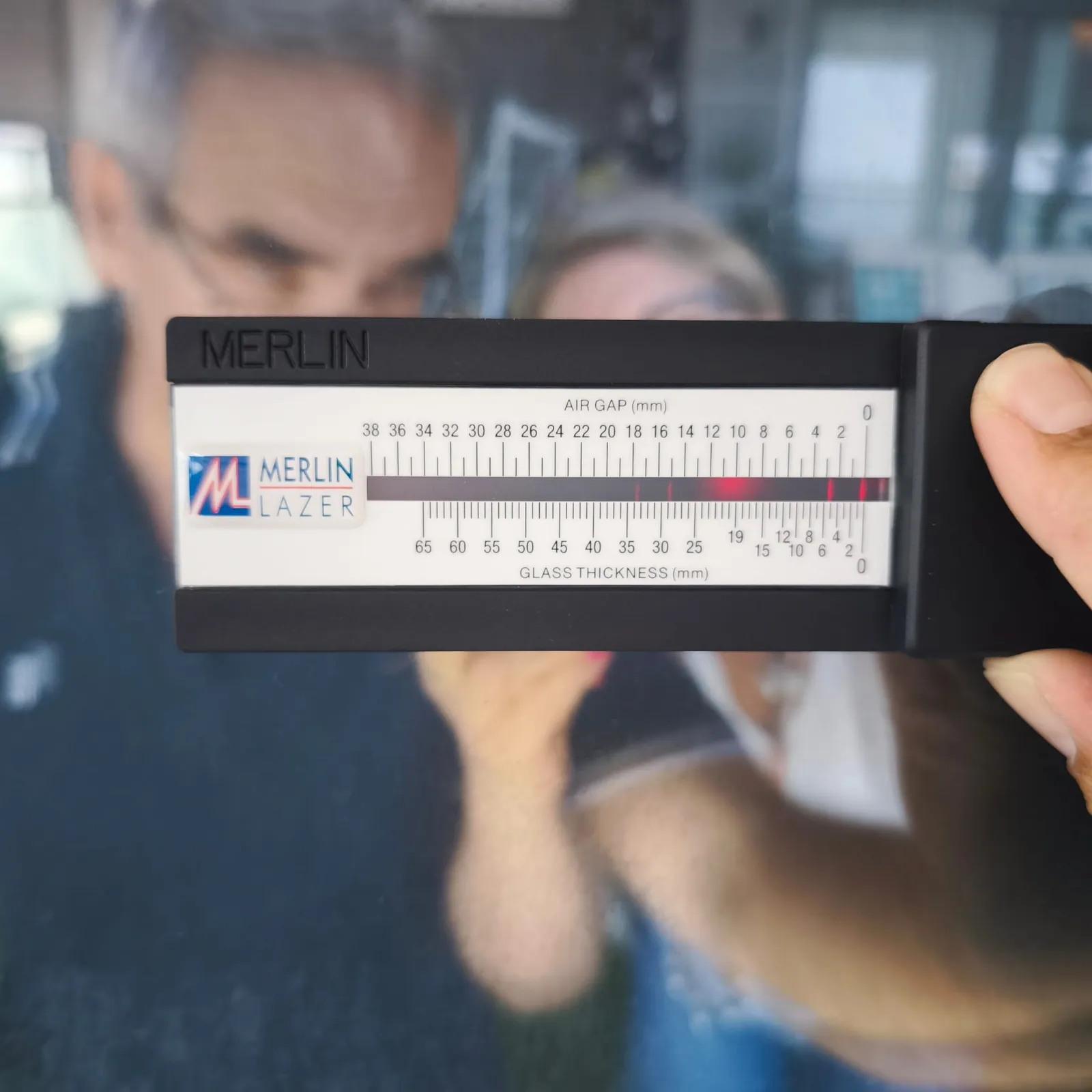 קריאת עובי הזכוכית ומרווח האוויר בסרגל - בדק בית סרגל מד עובי זכוכית ומרווח אוויר צמוד לזגוגית, עם השתקפויות הלייזר שמהן נקראים עובי הזכוכית ומרווח האוויר במילימטרים