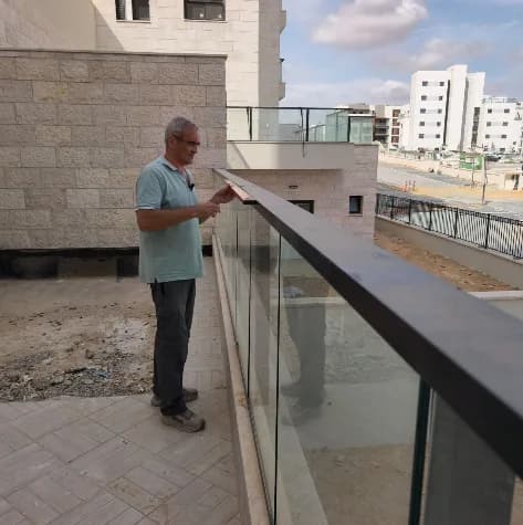 מומחה בדק בית בודק מעקה זכוכית ומאחז עליון במרפסת בית חדש בפרויקט תורן בלב השחר בדימונה - בדיקת חוזק, גובה ועיגון לפני מסירה