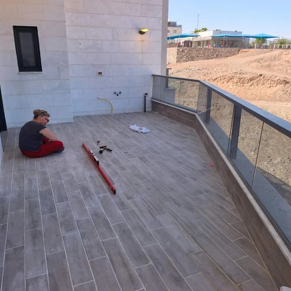מדידת שיפועים לאורך מרפסת השמש מומחית בדק בית מודדת שיפועי ניקוז בעזרת פלס ארוך לאורך מרפסת שמש גדולה בדירה - בדיקת ניקוז מים ממשטח מרוצף החשוף לגשם