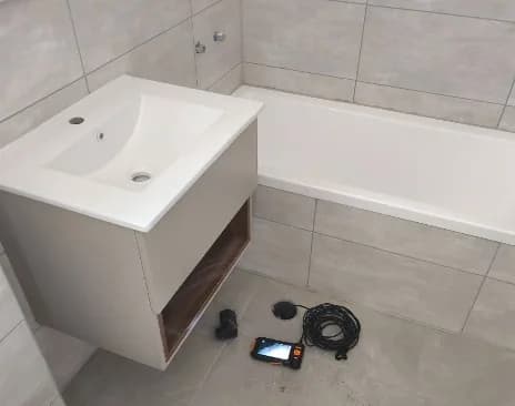 ערכת צילום קווים מונחת על רצפת חדר רחצה גמור בדירה חדשה עם ארון כיור ואמבטיה - בדיקת צנרת ניקוז לפני מסירה מקבלן