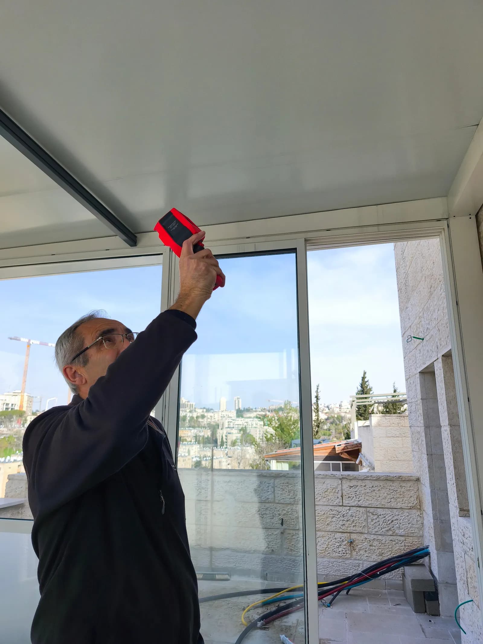 בדיקת תקרת מרפסת במד טמפרטורה מומחה בדק בית בודק תקרת מרפסת וחיבורי חלונות בעזרת מד טמפרטורה אינפרא אדום לאיתור גשרי קור וליקויי בידוד