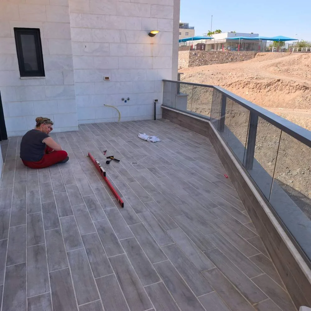 מומחית בדק בית מודדת שיפועי ניקוז בעזרת פלס ארוך לאורך מרפסת שמש גדולה בדירה - בדיקת ניקוז ממשטח מרוצף החשוף לגשם