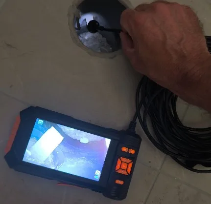 מומחה בדק בית מחדיר מצלמת צנרת אל מחסום רצפה סתום, והצג מציג את שאריות הבנייה שבתוך הקו - צילום קווים בבדיקת דירה אחרי בנייה