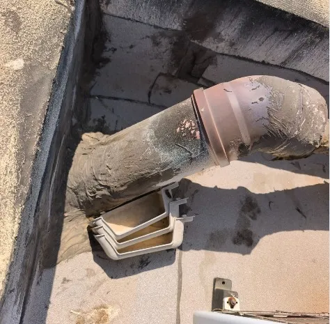 צינור מזגן מבודד החודר את שכבת האיטום בגג ללא שרוול מעבר וללא רולקת איטום, כשהבידוד סדוק ומתפורר והמעבר צמוד לקולטן הניקוז - ליקוי איטום שאותר בבדק בית